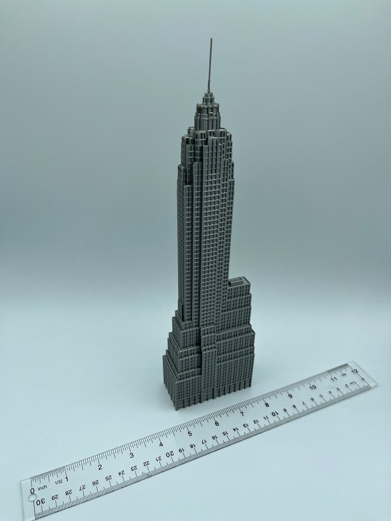 K&ouml;nnte beinhalten: Ein graues Miniaturmodell des Empire State Building mit detaillierter Fassade und Spitze. Ein Lineal liegt neben dem Modell und zeigt die Ma&szlig;e in Zentimetern an. Das Modell ist eine detaillierte Darstellung des ikonischen Wolkenkratzers.