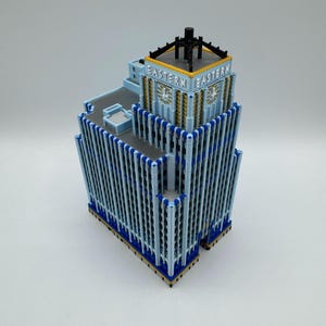 May include: A detailed model of a building with the word "EASTERN" on the top. The building is light blue with dark blue and gold accents. The model has a flat roof and a black structure on top.