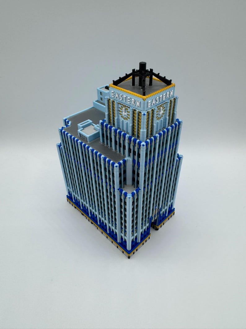 May include: A detailed model of a building with the word "EASTERN" on the top. The building is light blue with dark blue and gold accents. The model has a flat roof and a black structure on top.
