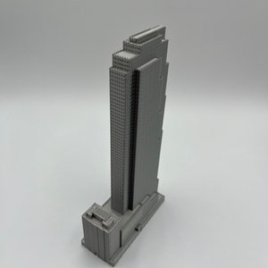 May include: A gray 3D printed model of a skyscraper with a rectangular base and a tall, narrow tower. The tower has a series of setbacks and a flat roof.