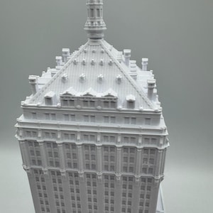 Puede incluir: Maqueta arquitect&oacute;nica blanca de un rascacielos. El modelo presenta intrincados detalles de ventanas y tejado, con una prominente aguja en la parte superior. La fachada del edificio est&aacute; cubierta de hileras de ventanas.