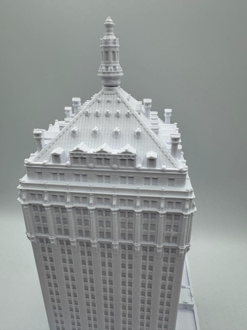 Puede incluir: Maqueta arquitect&oacute;nica blanca de un rascacielos. El modelo presenta intrincados detalles de ventanas y tejado, con una prominente aguja en la parte superior. La fachada del edificio est&aacute; cubierta de hileras de ventanas.