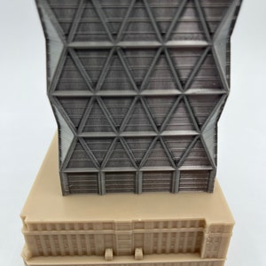 May include: A 3D printed model of a modern skyscraper with a geometric facade. The building is made of light grey plastic and has a beige base.
