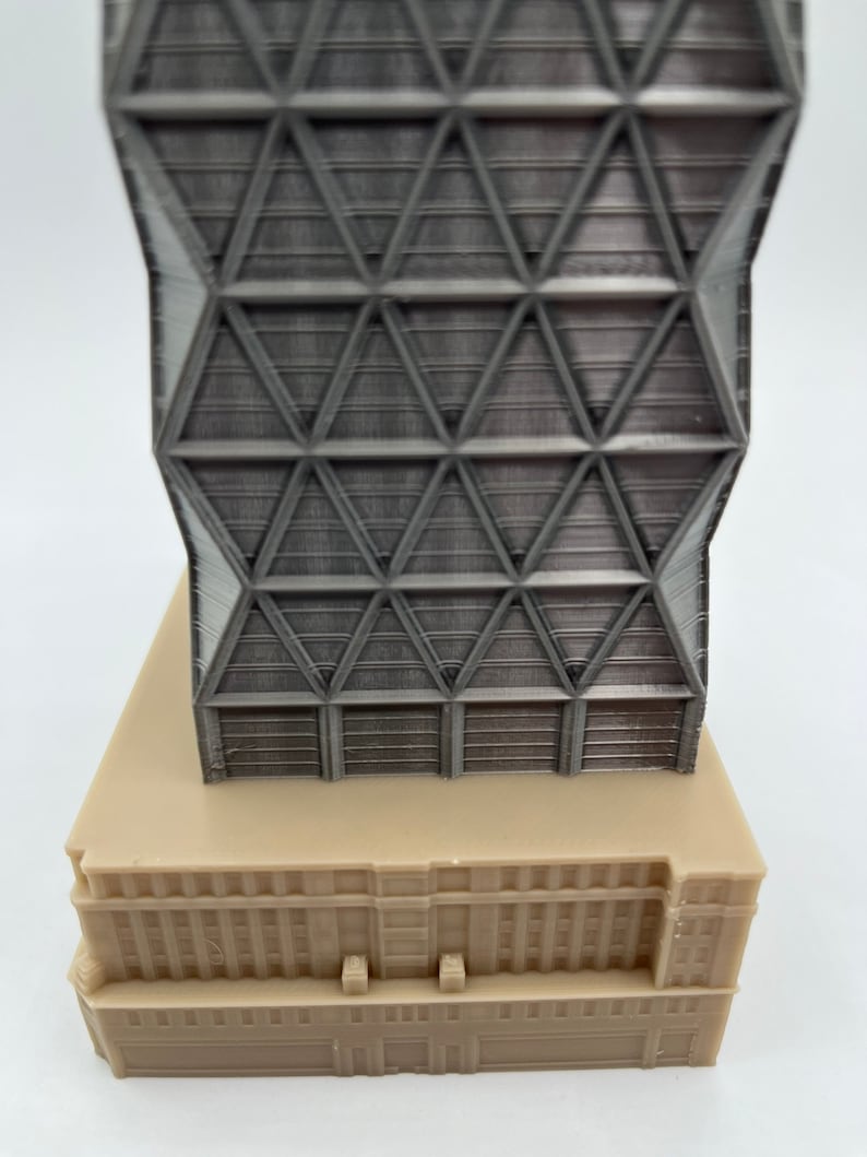 May include: A 3D printed model of a modern skyscraper with a geometric facade. The building is made of light grey plastic and has a beige base.