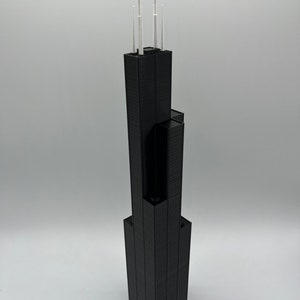 May include: A black 3D printed model of a skyscraper with white antenna details.