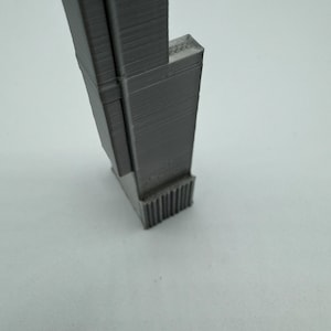Op de afbeelding: Een grijs 3D-geprint model van een hoog gebouw met een textuur en een basis met een decoratief ontwerp.
