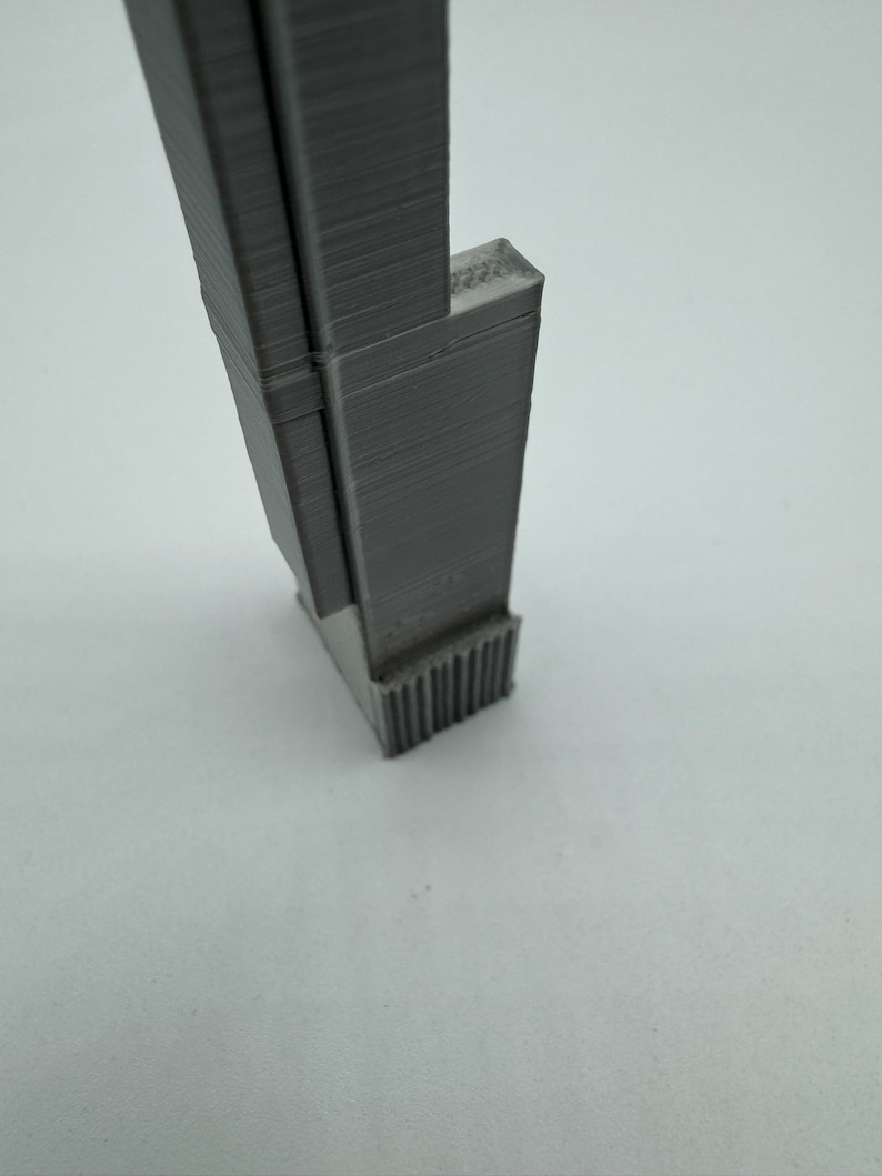 Op de afbeelding: Een grijs 3D-geprint model van een hoog gebouw met een textuur en een basis met een decoratief ontwerp.