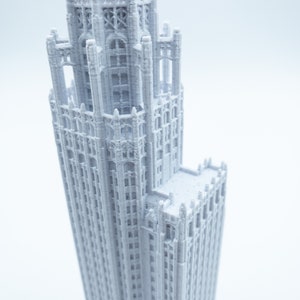 May include: A white 3D printed model of a tall, ornate building with a pointed roof and many windows.
