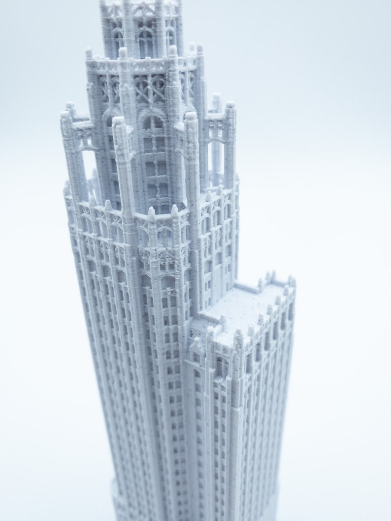 May include: A white 3D printed model of a tall, ornate building with a pointed roof and many windows.