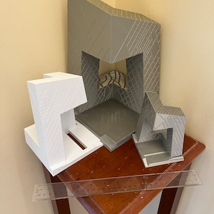 Peut inclure: Trois mod&egrave;les d'immeubles imprim&eacute;s en 3D, un gris et deux blancs, sont dispos&eacute;s sur une table en bois avec une r&egrave;gle. Les mod&egrave;les ont un motif g&eacute;om&eacute;trique.