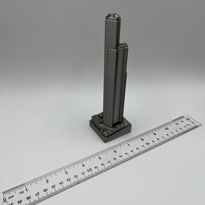 May include: A silver 3D printed model of a skyscraper, approximately 6 inches tall, with a ruler for scale.