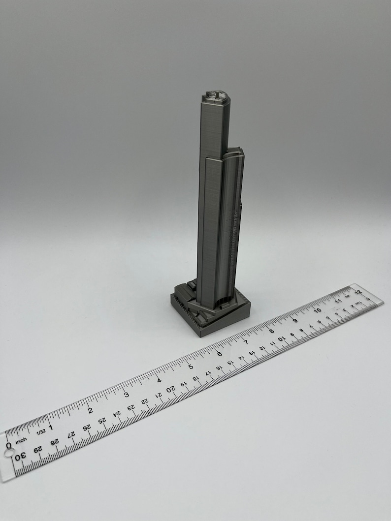 May include: A silver 3D printed model of a skyscraper, approximately 6 inches tall, with a ruler for scale.