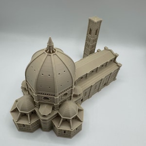 May include: A beige 3D-printed model of the Florence Cathedral, featuring the iconic dome, multiple smaller domes, and a separate bell tower. The model showcases architectural details and is set against a plain background.