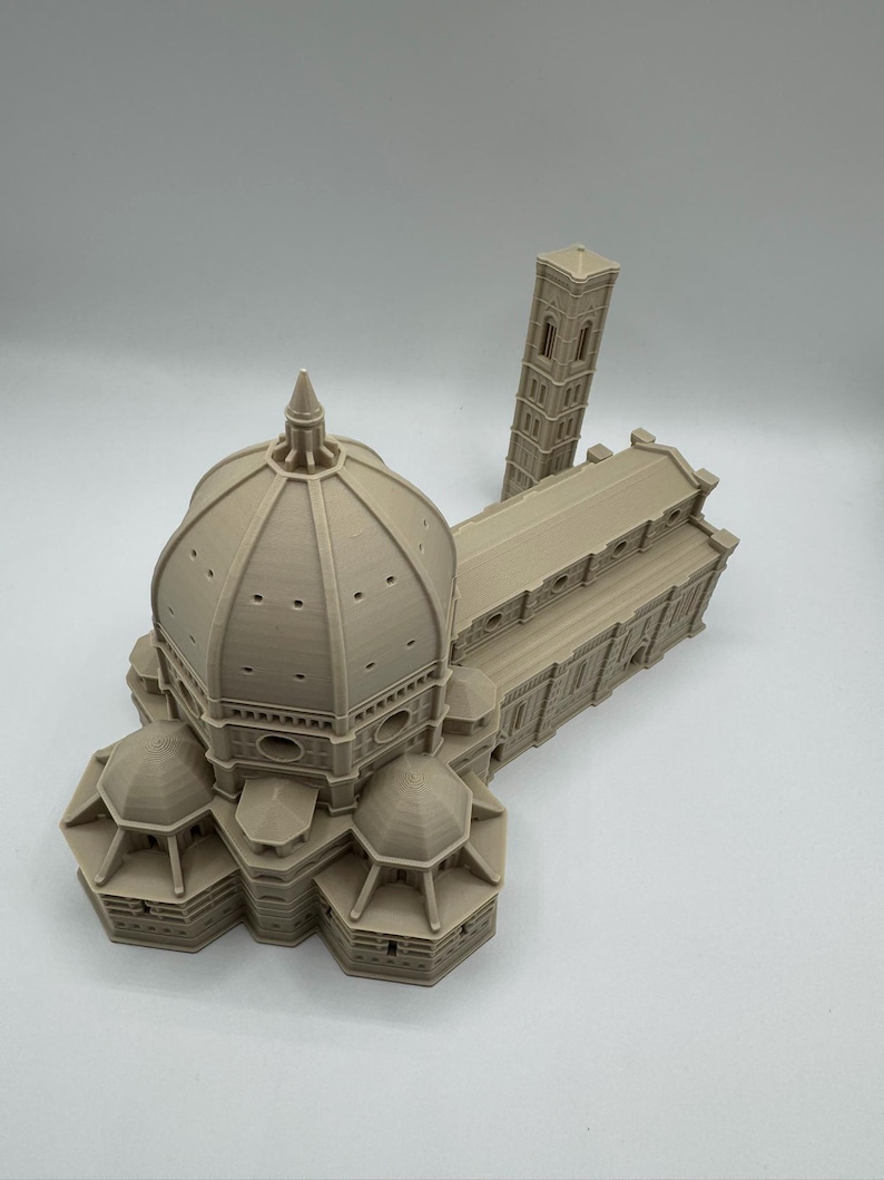 May include: A beige 3D-printed model of the Florence Cathedral, featuring the iconic dome, multiple smaller domes, and a separate bell tower. The model showcases architectural details and is set against a plain background.