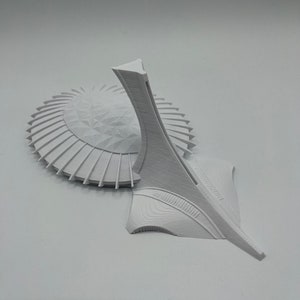May include: A white 3D printed model of the Olympic Stadium in Montreal, Canada. The model features the iconic tower and the surrounding stadium.
