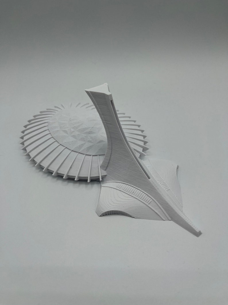 May include: A white 3D printed model of the Olympic Stadium in Montreal, Canada. The model features the iconic tower and the surrounding stadium.