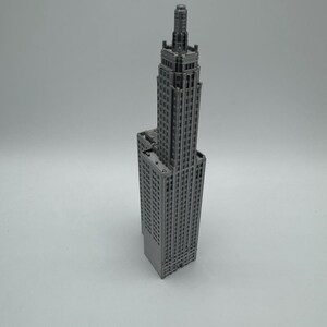 May include: A grey model of a tall, slender skyscraper with a pointed roof and many windows.