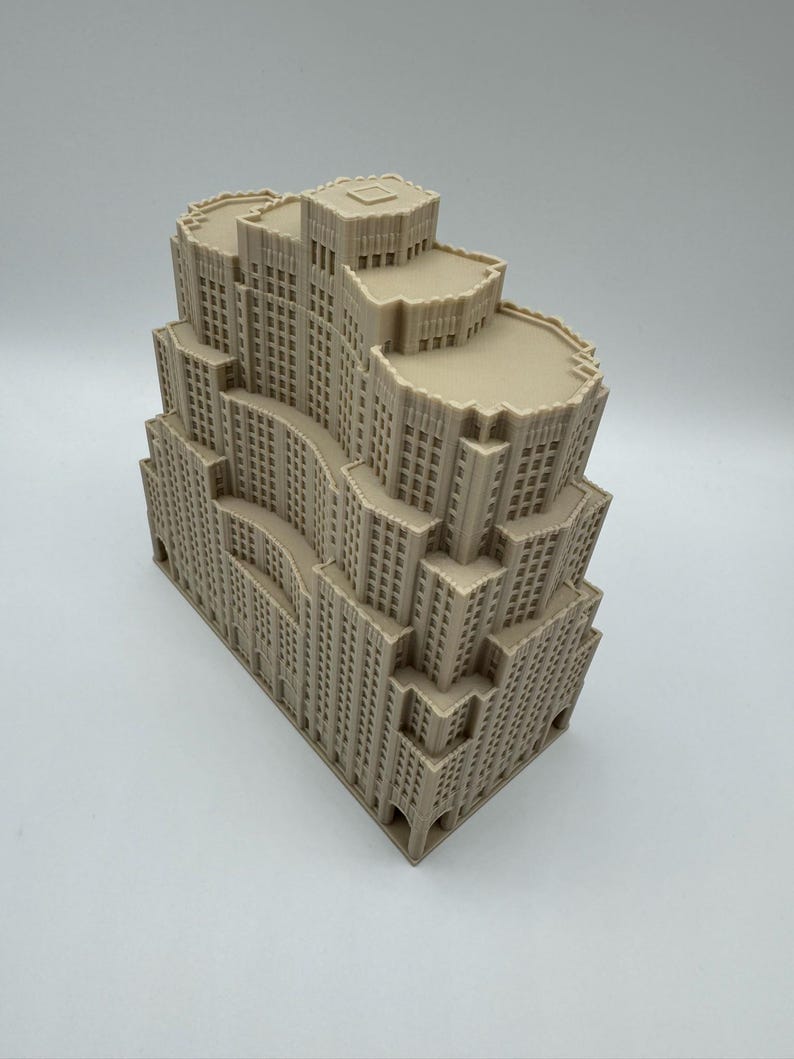 May include: A beige architectural model of a multi-tiered skyscraper. The model has detailed windows and a stepped design, with a flat roof. The building's facade has a textured appearance, and the overall design is reminiscent of Art Deco architecture.