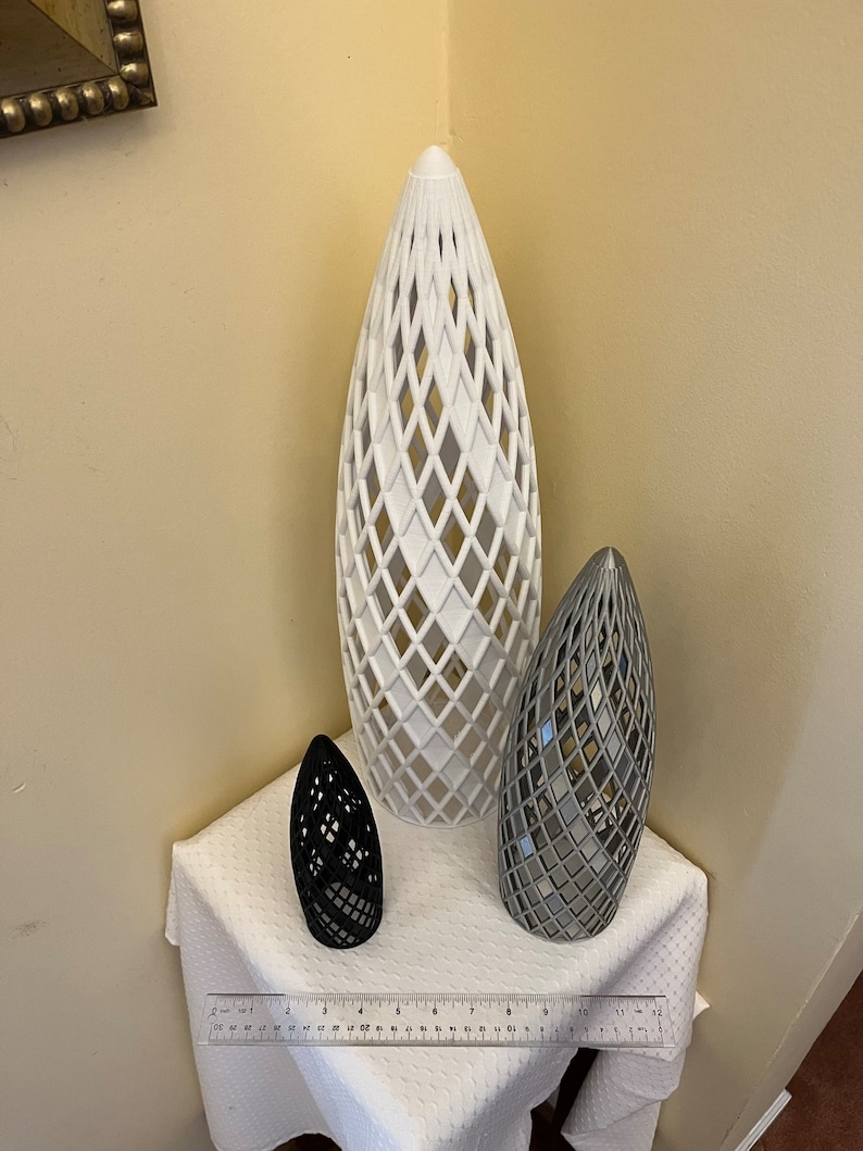 May include: Three decorative, geometric, 3D printed vases. The largest vase is white, the medium vase is gray, and the smallest vase is black.