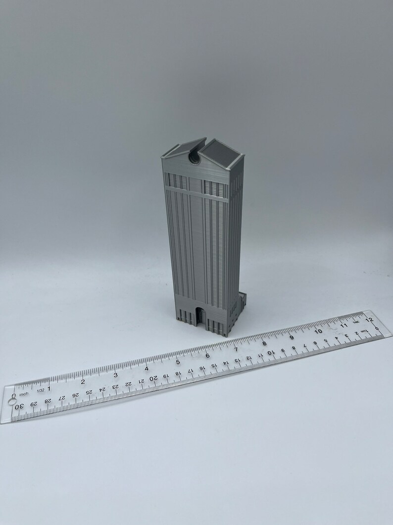May include: A 3D printed model of a tall, gray building with a flat roof and a small opening at the top. The model is about 6 inches tall and is sitting on a white surface.