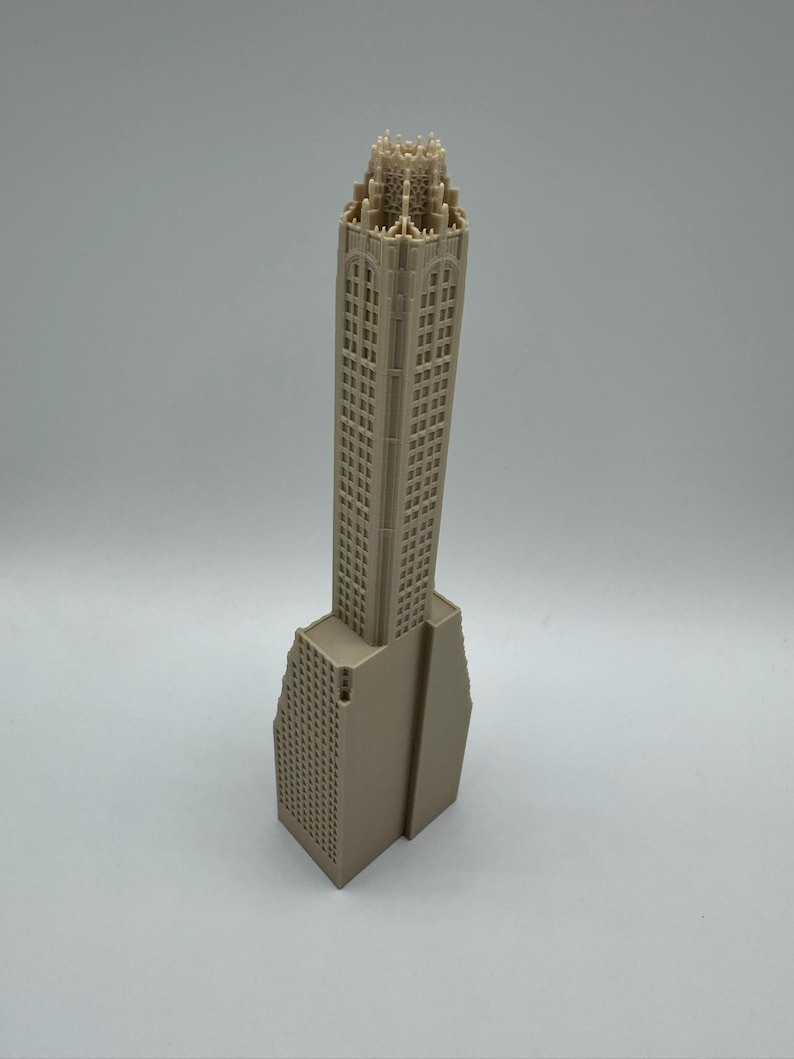 May include: A beige architectural model of a skyscraper. The building features a detailed facade with numerous windows and a decorative top. The base of the building has a unique, angled design. The model is set against a plain white background.