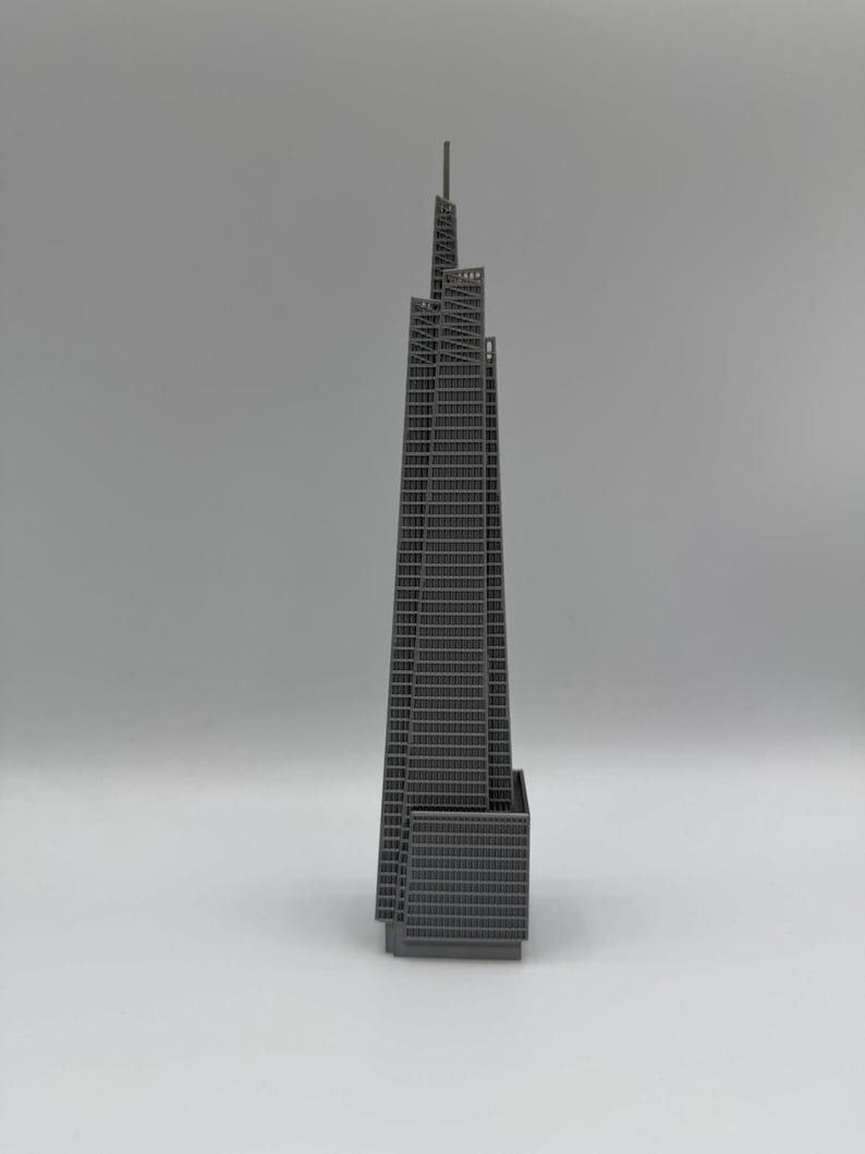 May include: A gray architectural model of a skyscraper. The building has a rectangular base and a tall, tapered tower with a spire. The facade features a grid-like pattern of windows. The model is set against a plain gray background.