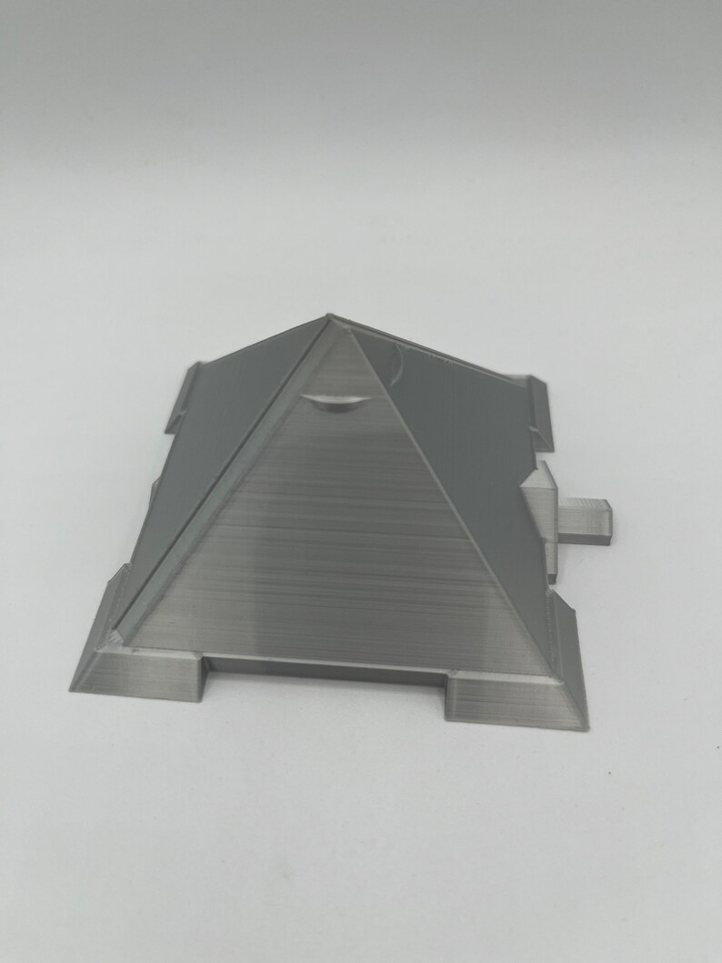Puede incluir: Modelo de pir&aacute;mide gris impreso en 3D con parte superior plana y base rectangular. La pir&aacute;mide tiene una superficie texturizada y est&aacute; dise&ntilde;ada con detalles arquitect&oacute;nicos. El modelo es una forma geom&eacute;trica s&oacute;lida.