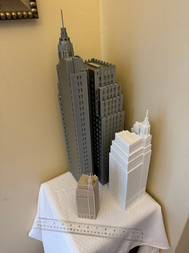 Pu&ograve; includere: Tre edifici modello stampati in 3D, uno grigio, uno bianco e uno beige, sono disposti su una tovaglia bianca. Un righello si trova in primo piano.