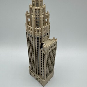 May include: A beige 3D printed architectural model of a skyscraper featuring intricate gothic-style detailing, a tiered tower structure, multiple vertical window columns, and a stepped roof design with decorative pinnacles and arched window frames.