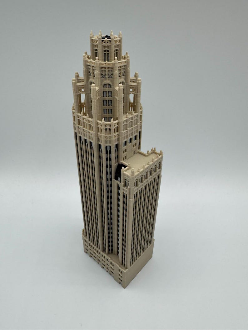 May include: A beige 3D printed architectural model of a skyscraper featuring intricate gothic-style detailing, a tiered tower structure, multiple vertical window columns, and a stepped roof design with decorative pinnacles and arched window frames.