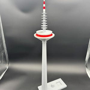May include: A white and red model of a radio tower. The tower has a cylindrical base and a series of stacked, disc-shaped elements. The top section is white with red stripes. The model is on a white rectangular base.