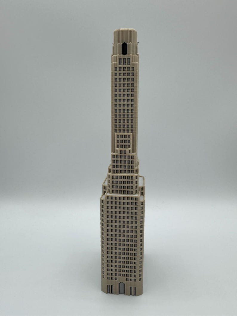May include: A beige, three-dimensional model of a skyscraper featuring a stepped architectural design. The structure displays a repeating pattern of rectangular windows across its vertical facade, culminating in a narrow, tiered tower section.