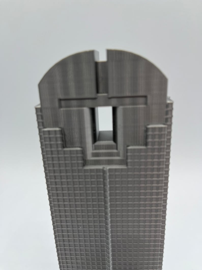 May include: A grey 3D printed model of a skyscraper with a distinctive design at the top. The building has a grid pattern on the facade.