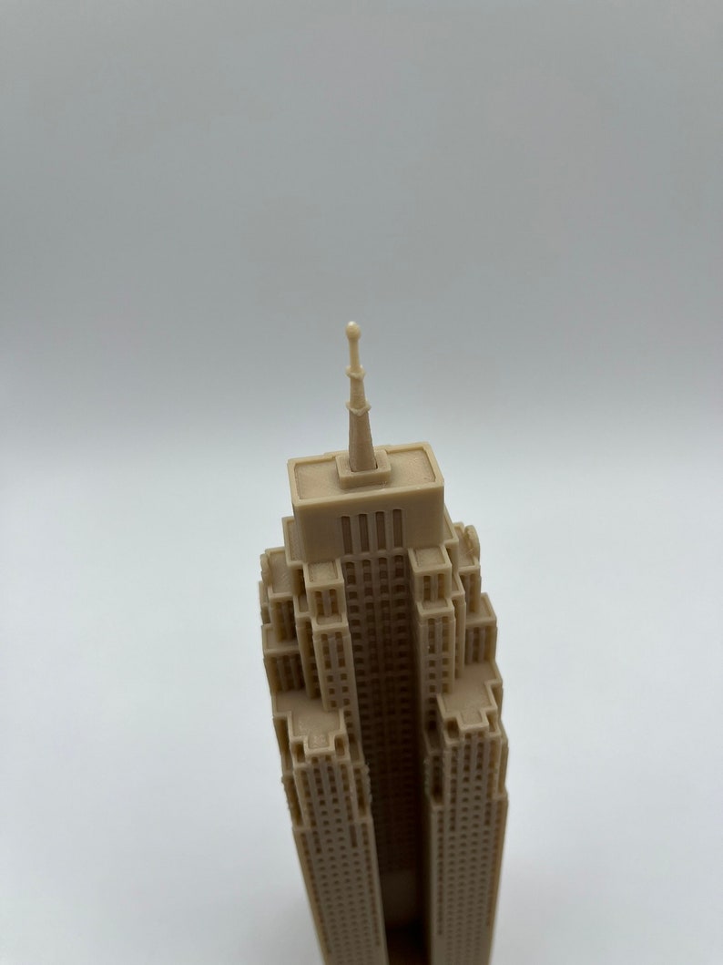 May include: A beige miniature model of a skyscraper with a pointed top. The model is made of plastic and has a detailed facade.