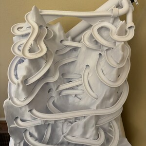May include: White 3D printed marble run with a complex track design. The track is made of multiple levels and curves, and it includes a starting point and a finish line.