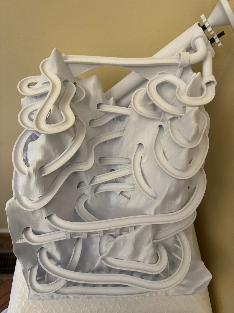 May include: White 3D printed marble run with a complex track design. The track is made of multiple levels and curves, and it includes a starting point and a finish line.