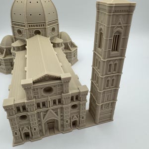 May include: A beige 3D-printed model of the Florence Cathedral, featuring the iconic dome, facade, and bell tower. The model showcases architectural details, including arched windows and intricate rooflines. The model is a detailed replica of the famous Italian landmark.