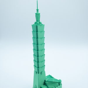 May include: A green 3D printed model of a skyscraper. The building has a unique design with a pointed top and a series of stepped levels.