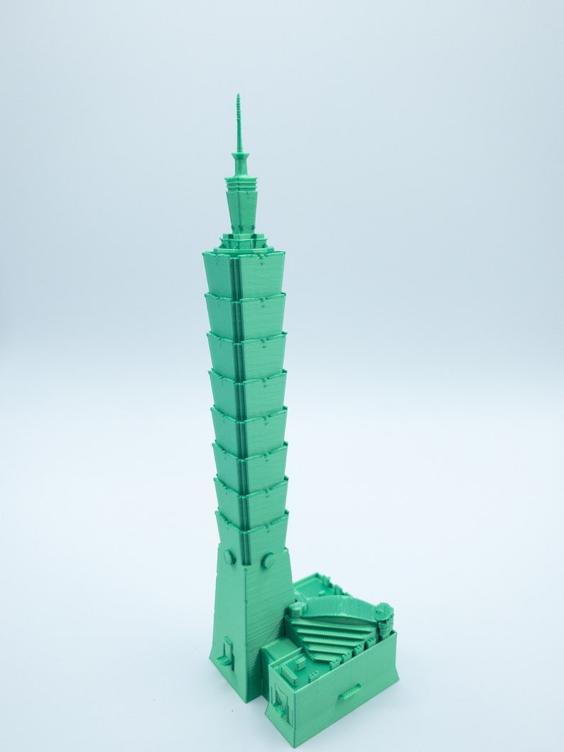 May include: A green 3D printed model of a skyscraper. The building has a unique design with a pointed top and a series of stepped levels.