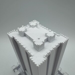 May include: White 3D printed model of a tall building with a crenellated roof and walls. The building has a square base and is made of a smooth, white plastic.