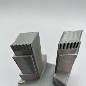 Op de afbeelding: Een 3D-geprint model van een paar wolkenkrabbers met een grijze afwerking.