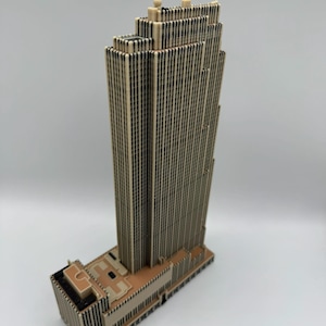 Puede incluir: Maqueta arquitect&oacute;nica beige y negra de un rascacielos. El modelo presenta un dise&ntilde;o escalonado con m&uacute;ltiples l&iacute;neas verticales que representan ventanas. La base del edificio es de un tono beige m&aacute;s claro.