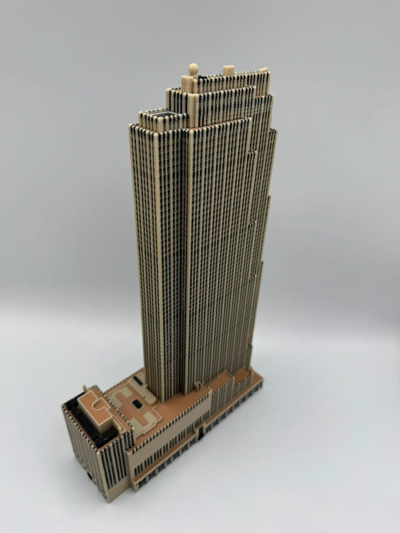 Puede incluir: Maqueta arquitect&oacute;nica beige y negra de un rascacielos. El modelo presenta un dise&ntilde;o escalonado con m&uacute;ltiples l&iacute;neas verticales que representan ventanas. La base del edificio es de un tono beige m&aacute;s claro.