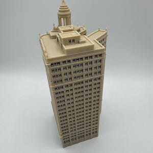 Op de afbeelding: Een beige miniatuurmodel van een hoog gebouw met een koepelvormig dak en veel ramen.