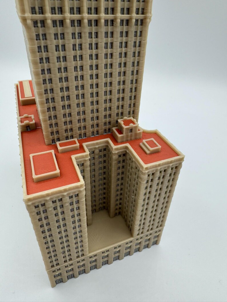May include: A beige and red architectural model of a skyscraper. The model features multiple rectangular sections with numerous small, dark windows. The roof is a vibrant red, and the overall design is highly detailed.
