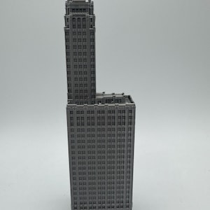 May include: A grey 3D printed model of a tall skyscraper building with many windows.