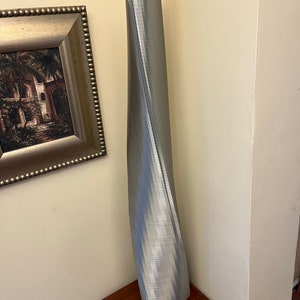 Op de afbeelding: Een zilverkleurig, 3D-geprint model van een hoog, draaiend gebouw. Het model staat op een houten tafel.