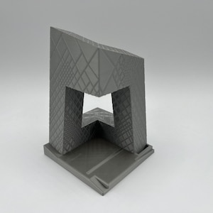 Peut inclure: Mod&egrave;le 3D imprim&eacute; en gris d'un b&acirc;timent avec un design g&eacute;om&eacute;trique unique. Le b&acirc;timent a une grande ouverture au centre et une petite base.