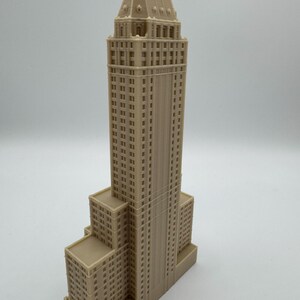 Może przedstawiać: Szczeg&oacute;łowa, beżowa miniatura wieżowca. Model charakteryzuje się wielopoziomową konstrukcją z licznymi oknami i detalami architektonicznymi. Fasada budynku ma jednolity beżowy kolor i stoi na gładkim tle.