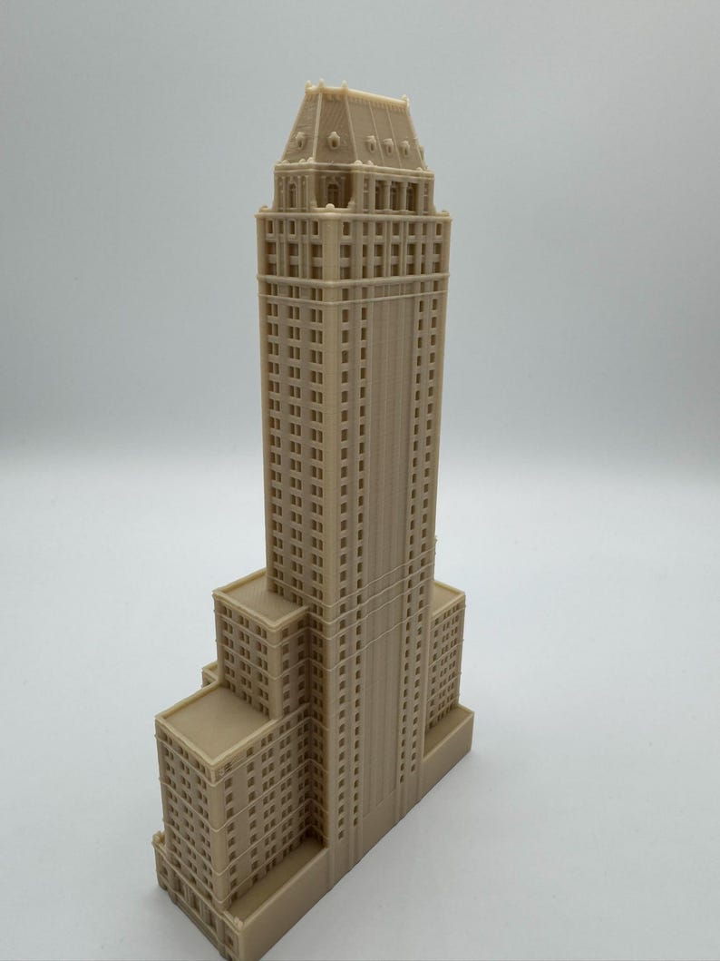 Może przedstawiać: Szczeg&oacute;łowa, beżowa miniatura wieżowca. Model charakteryzuje się wielopoziomową konstrukcją z licznymi oknami i detalami architektonicznymi. Fasada budynku ma jednolity beżowy kolor i stoi na gładkim tle.